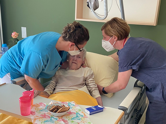 Zwei Pflegekräfte beugen sich über ein Bett und helfen einer Patientin, 3 Jahre Diakonie Hospiz Woltersdorf, Nachrichten, Diakonie-Hospiz Woltersdorf