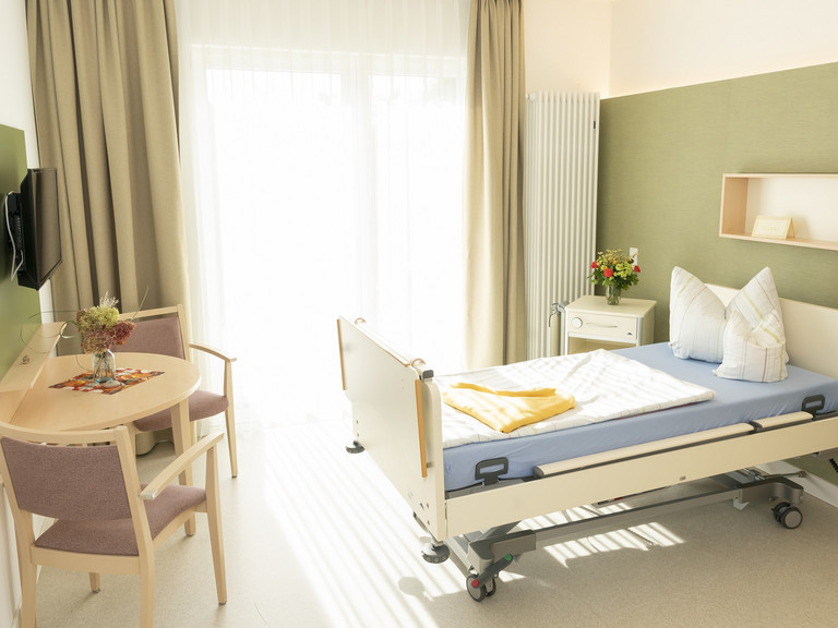 Gästezimmer im Hospiz mit Gästebett, Sitzmöbel und bodentiefen Fenster - Diakonie Hospiz Woltersdorf
