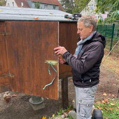 Eine ehrenamtlich engagierter Mann arbeitet an der hölzernen Außentür der Hühnervoliere im Hühnergarten des Diakonie Hospiz Woltersdorf.