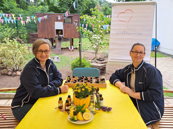 Zwei Mitarbeiterinnen sitzen an Gartentisch, im Hintergrund ist das Hühnerhaus