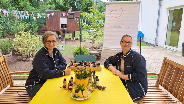 Zwei Mitarbeiterinnen sitzen am Gartentisch - Im Hintegrrund ist Hühnerhaus - Diakonie Hospiz Woltersdorf