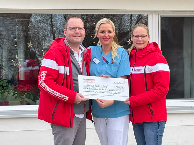 Hospiz-Mitarbeiterin (Mitte) nimmt Spendenscheck von der Hauskrankenpflege Vetter entgegen