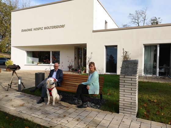 Geschäftsführer Walther Seiler und Pflegedienstleitung Stefanie Micklitza mit Hund Julius auf einer Bank vor dem Hospiz.