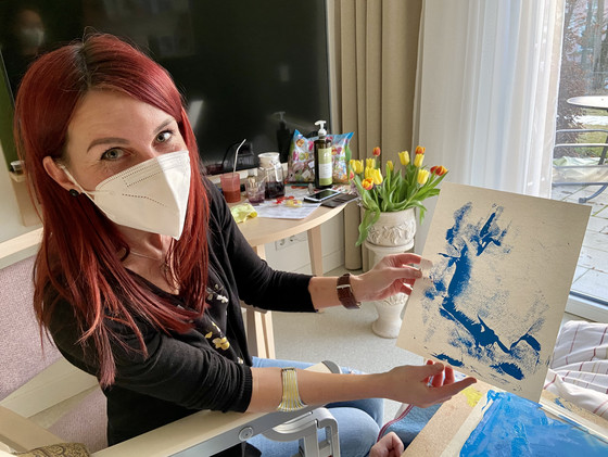 Das Bild zeigt eine Frau mit einer Maske. Sie malt gemeinsam mit den Hospizgästen. Das Bild zeigt eine Frau mit einer Maske. Sie malt gemeinsam mit den Hospizgästen.