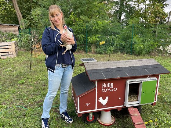 Eine Frau hält ein Huhn in der Hand in eine Garten mit Hühnerstall, Nachrichten, Diakonie Hospiz Woltersdorf